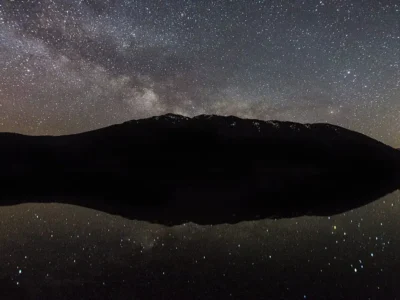 Via Láctea sobre montanha com reflexo em lago durante a noite