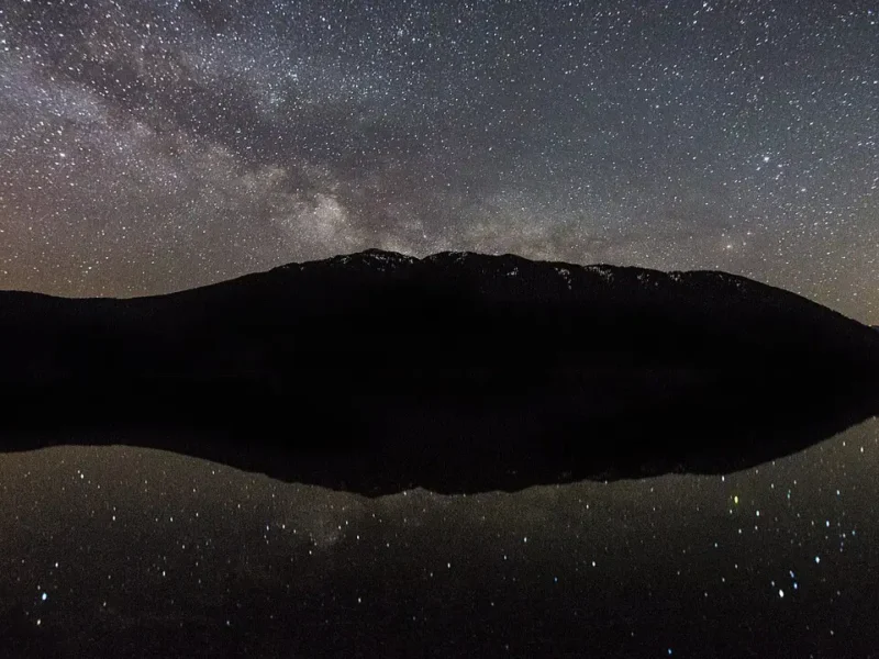 Via Láctea sobre montanha com reflexo em lago durante a noite
