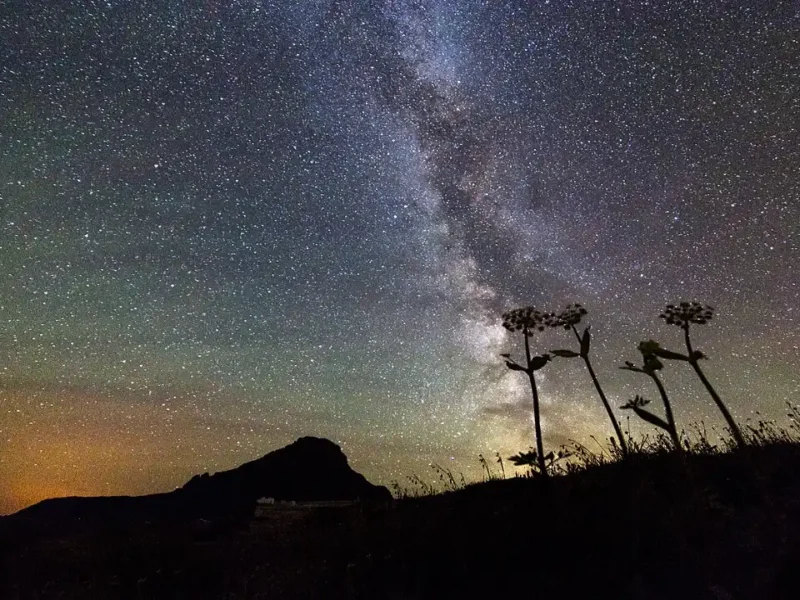 Céu estrelado com a Via Láctea sobre uma paisagem montanhosa durante a noite