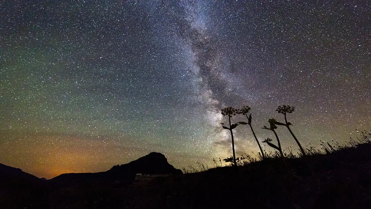 Céu estrelado com a Via Láctea sobre uma paisagem montanhosa durante a noite