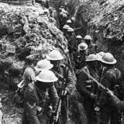 Soldados britânicos em uma trincheira enlameada na Bélgica, durante a Primeira Guerra Mundial, cercados por sacos de areia e equipamentos militares.