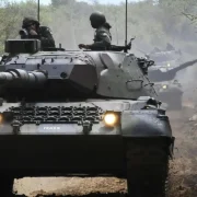 Carro de combate Leopard 1A5 BR do Exército Brasileiro visto de frente, com militares na torre, durante deslocamento por estrada de terra.