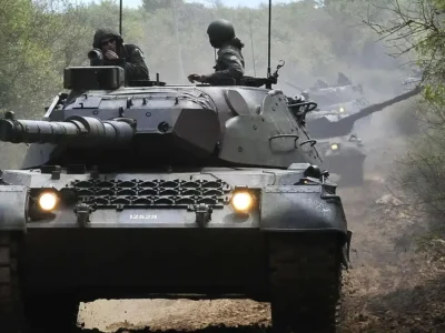 Carro de combate Leopard 1A5 BR do Exército Brasileiro visto de frente, com militares na torre, durante deslocamento por estrada de terra.