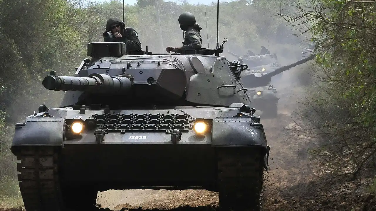 Carro de combate Leopard 1A5 BR do Exército Brasileiro visto de frente, com militares na torre, durante deslocamento por estrada de terra. Carro de combate Leopard 1A5 BR do Exército Brasileiro visto de frente, com militares na torre, durante deslocamento por estrada de terra.