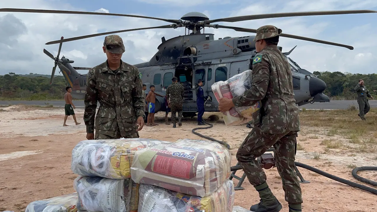 Militares do Exército Brasileiro movimentam suprimentos embalados ao lado de um helicóptero militar em uma área de pouso. Militares do Exército Brasileiro movimentam suprimentos embalados ao lado de um helicóptero militar em uma área de pouso.