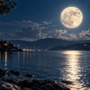 Lua cheia iluminando uma paisagem costeira com montanhas e reflexo sobre a água