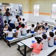 Crianças realizando atividades escolares em mesas coloridas dentro de uma sala de aula.