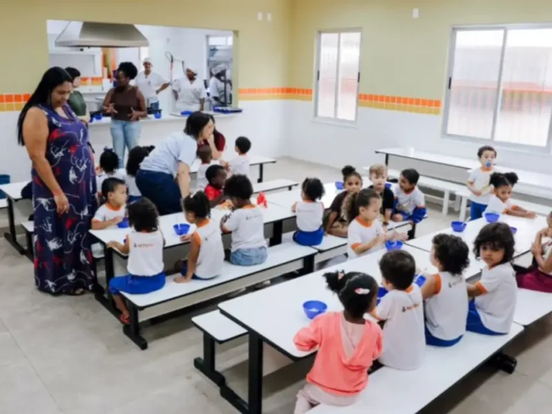 Crianças realizando atividades escolares em mesas coloridas dentro de uma sala de aula.