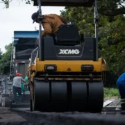 Rolo compactador trabalha na pavimentação de uma rua do Retiro São Joaquim, em Itaboraí, enquanto operários executam serviços de infraestrutura.