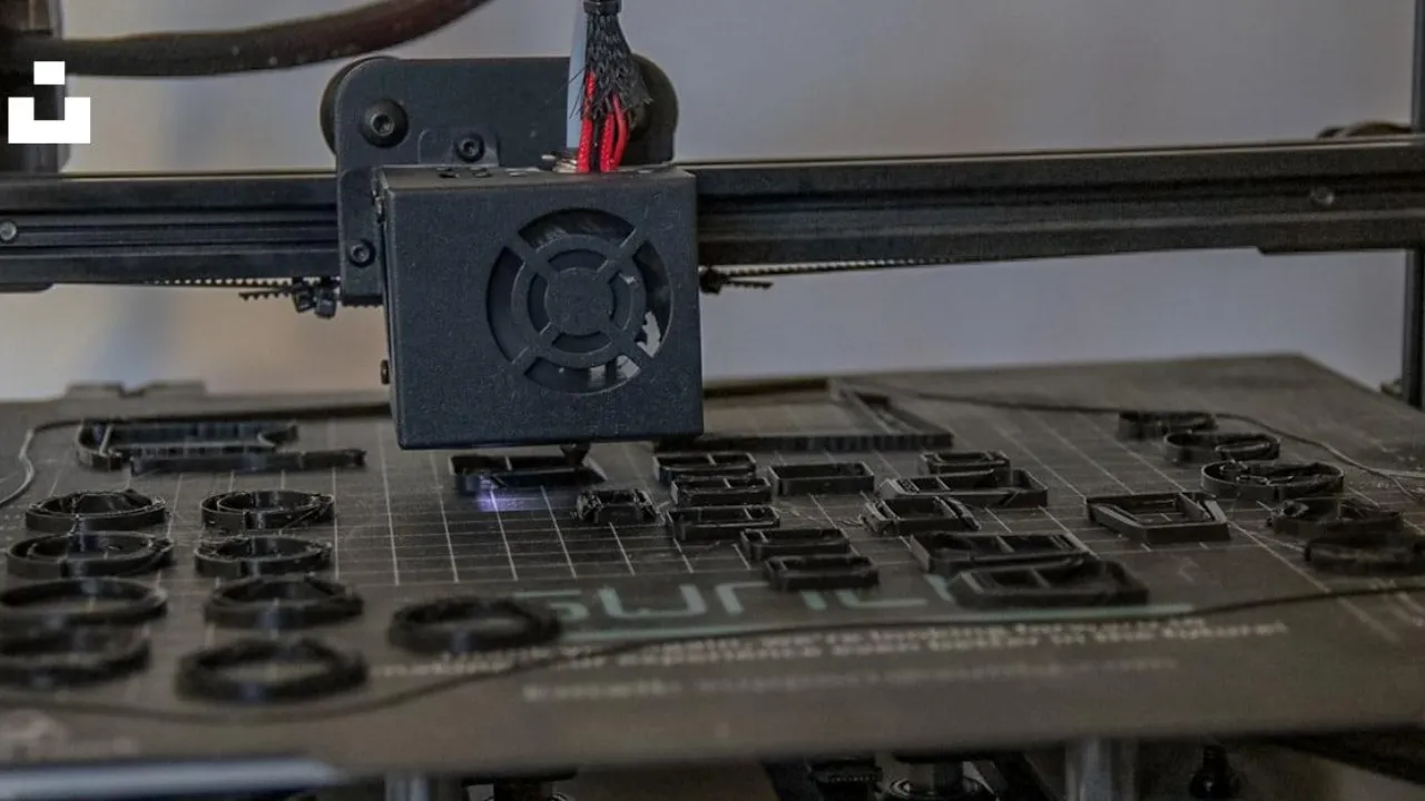 Impressora 3D em funcionamento, com cabeçote depositando plástico sobre uma peça em fabricação.