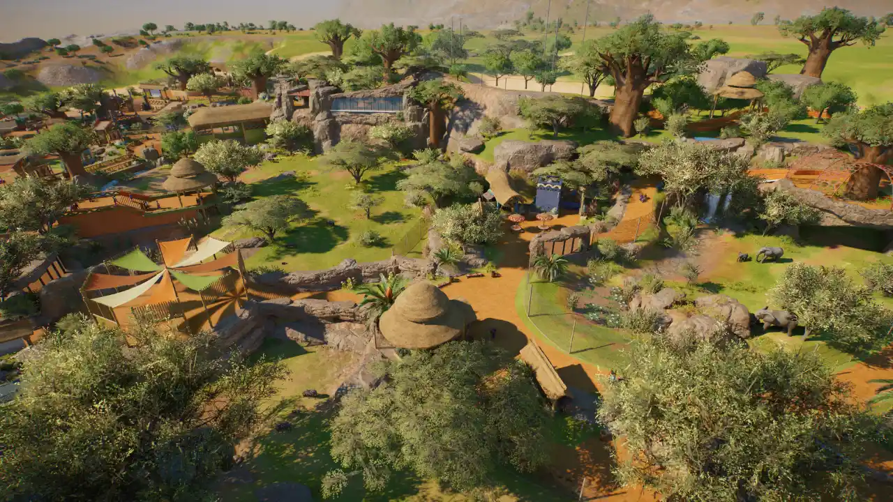 Vista aérea de zoológico em Planet Zoo 2 com árvores, caminhos, formações rochosas, abrigos e recintos de animais.