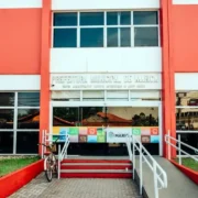 Fachada da Prefeitura Municipal de Maricá, com arquitetura em tons de vermelho e branco, jardins e calçada arborizada.