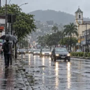 Pedestre com guarda-chuva caminha sob chuva em rua molhada