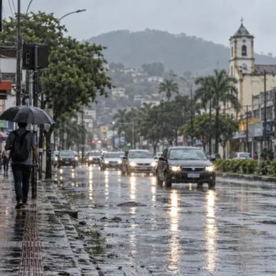 Pedestre com guarda-chuva caminha sob chuva em rua molhada