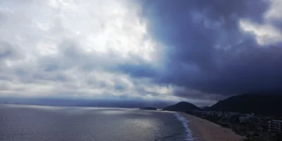 Praia de Piratininga, em Niterói, com nuvens escuras no céu, ilustrando a previsão de chuva e ventos fortes.