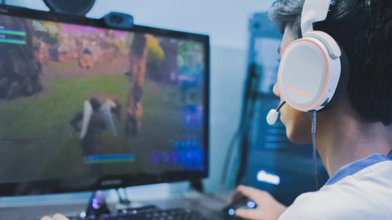 Jogador usa headset e controle diante de monitor durante partida de videogame