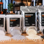 Embalagens de Prusament Pellets dos materiais PLA, PETG, ASA e PC Blend, acompanhadas de grânulos plásticos utilizados na impressão 3D de grande formato.