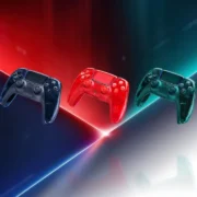 Três controles DualSense transparentes para PS5 nas cores cinza-grafite, laranja-avermelhado e verde-esmeralda, apresentados sobre fundo iluminado.