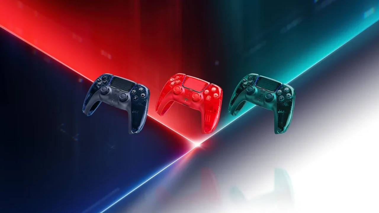Três controles DualSense transparentes para PS5 nas cores cinza-grafite, laranja-avermelhado e verde-esmeralda, apresentados sobre fundo iluminado.