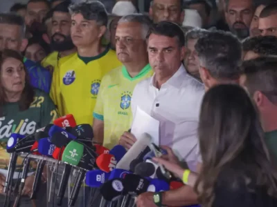 Flávio Bolsonaro, de camisa branca, durante entrevista coletiva cercado por jornalistas, microfones e apoiadores após o segundo turno das Eleições 2026.