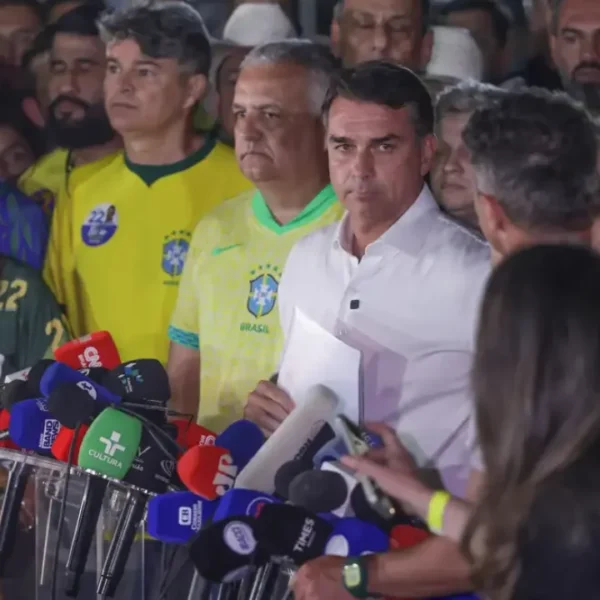 Flávio Bolsonaro, de camisa branca, durante entrevista coletiva cercado por jornalistas, microfones e apoiadores após o segundo turno das Eleições 2026.