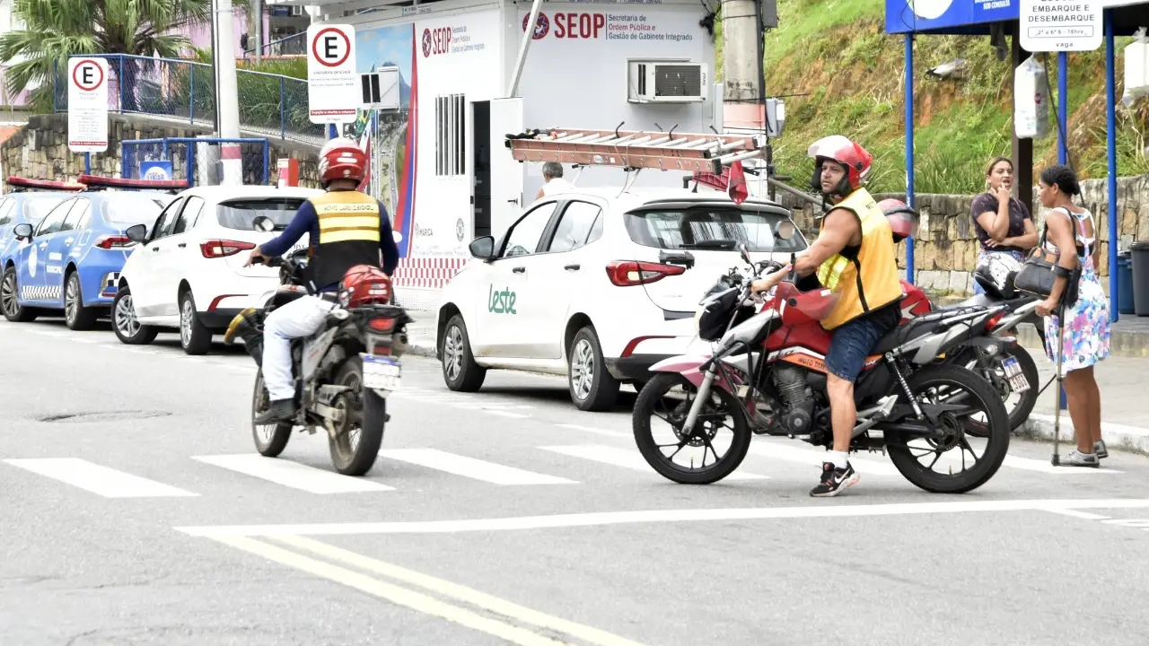 Dois motociclistas em uma via pública de Maricá, próximos a veículos municipais e a uma unidade da Secretaria de Ordem Pública. Dois motociclistas em uma via pública de Maricá, próximos a veículos municipais e a uma unidade da Secretaria de Ordem Pública.