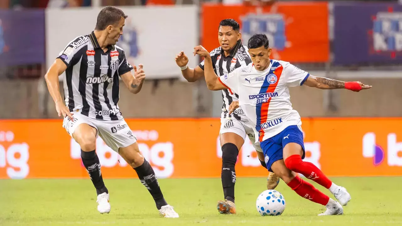 Jogador do Bahia disputa a bola com dois atletas do Santos durante partida do Campeonato Brasileiro.