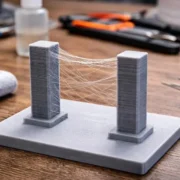 Duas torres de teste impressas em 3D apresentam fios finos de plástico entre elas, defeito conhecido como stringing.
