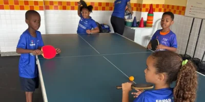 Raquete e bola de tênis de mesa sobre uma mesa azul, em ambiente interno.