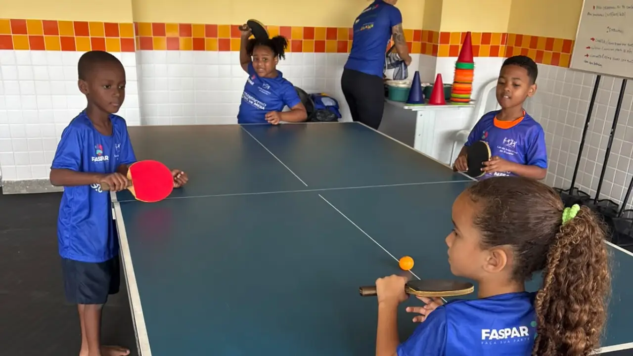 Raquete e bola de tênis de mesa sobre uma mesa azul, em ambiente interno.