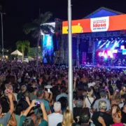 Público acompanha apresentação musical noturna ao ar livre, com iluminação de palco e pessoas reunidas diante do show.