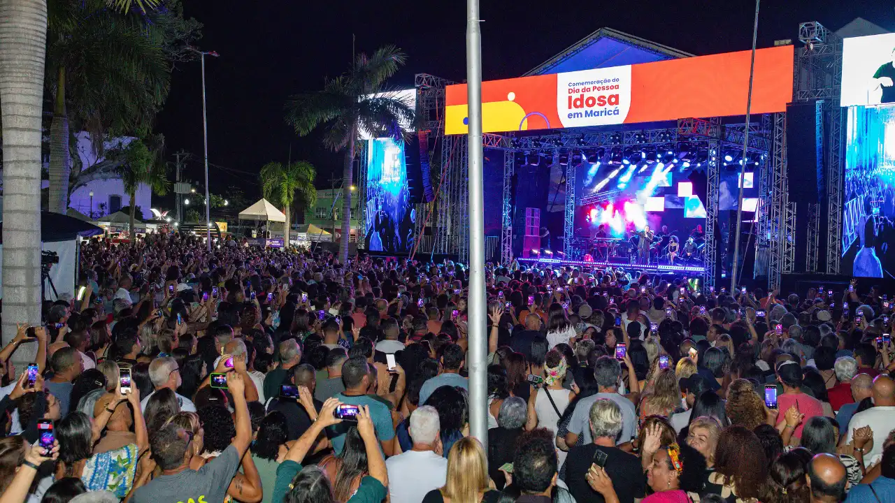 Público acompanha apresentação musical noturna ao ar livre, com iluminação de palco e pessoas reunidas diante do show.