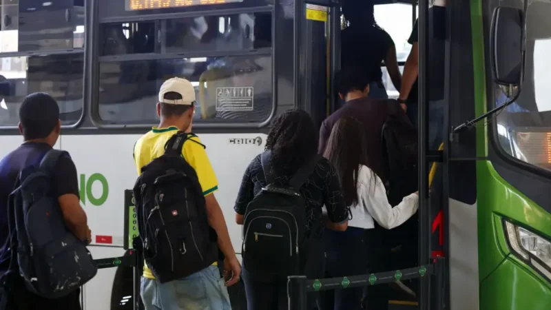 Passageiros com mochilas embarcam em ônibus urbano durante movimentação em ponto de transporte público.