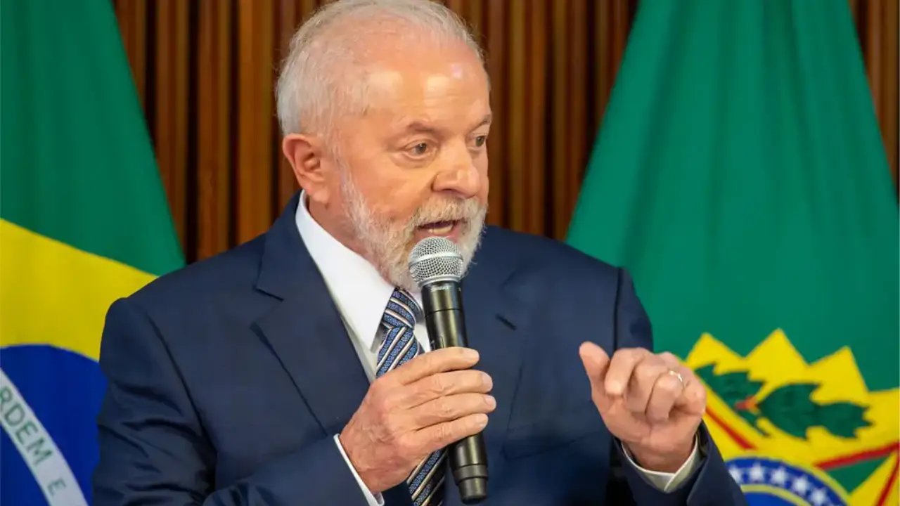 Presidente Lula discursa ao microfone, usando terno azul e gravata, diante de bandeiras do Brasil. Presidente Lula discursa ao microfone, usando terno azul e gravata, diante de bandeiras do Brasil.