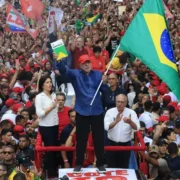 Presidente Lula ergue a bandeira do Brasil e um exemplar da Constituição diante de uma multidão de apoiadores durante ato de campanha.