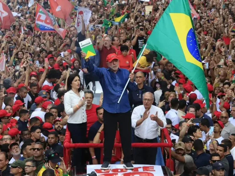 Presidente Lula ergue a bandeira do Brasil e um exemplar da Constituição diante de uma multidão de apoiadores durante ato de campanha.