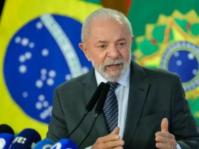 Pronunciamento diante de microfones, com bandeiras do Brasil ao fundo, em cerimônia oficial.