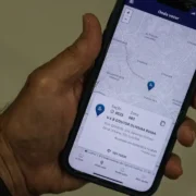Pessoa segura celular com aplicativo e-Título aberto na função Onde votar, mostrando mapa e endereço da seção eleitoral.