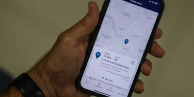 Pessoa segura celular com aplicativo e-Título aberto na função Onde votar, mostrando mapa e endereço da seção eleitoral.